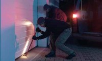 burglar attempting to break into a garage door with crowbar at night